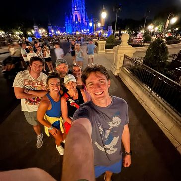 Group selfie at night in front of a brightly lit castle at a theme park.