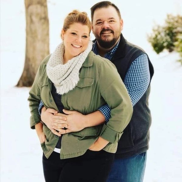 Smiling couple embraces outdoors in winter with snow and trees.
