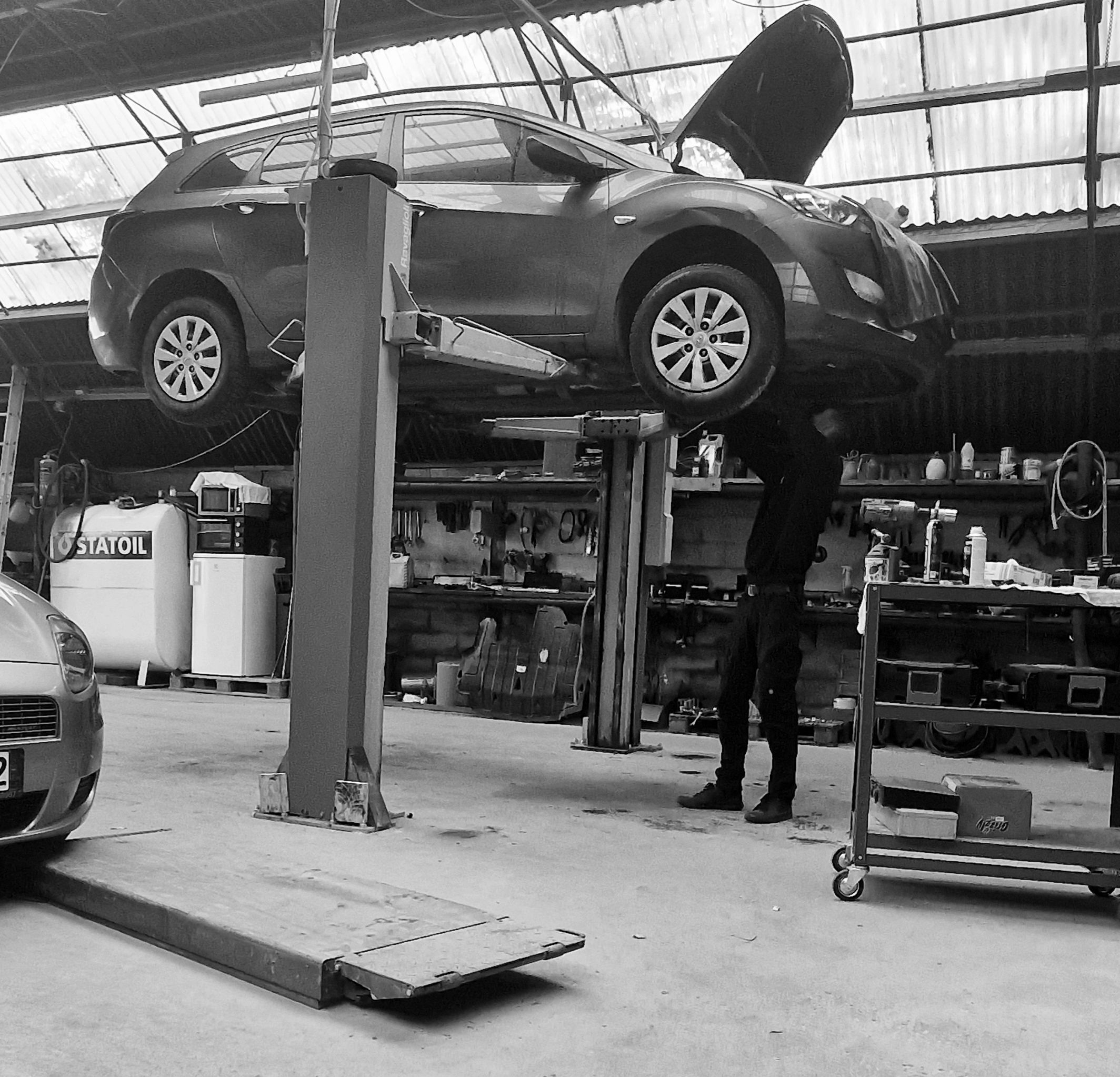 Car lifted on a hydraulic lift in a garage with a mechanic working under the hood.