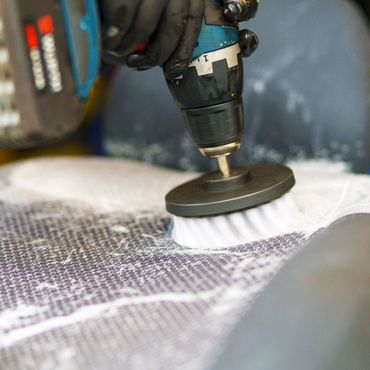 Close-up of a drill with a brush attachment cleaning a textured surface.