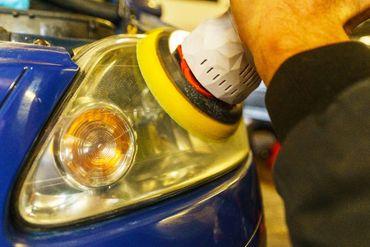 Person polishing a car's headlight with a machine buffer.