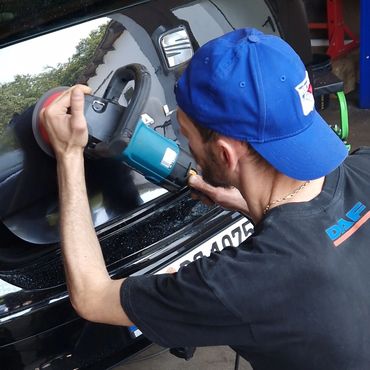 Man polishing a black car's rear with a power buffer.