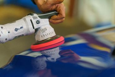 Person polishing a blue car with a rotary buffer.