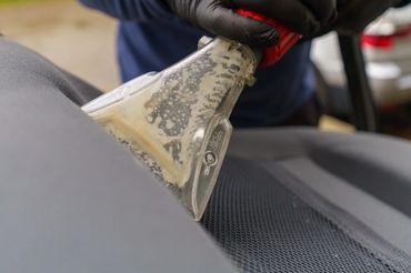 Person cleaning a car seat with a specialized upholstery tool.