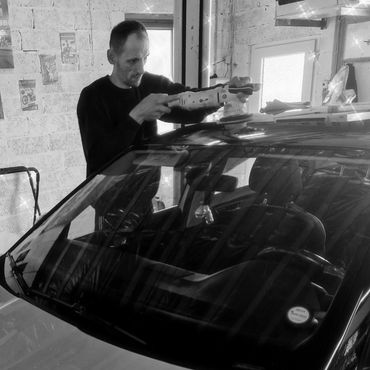 Man polishing a car roof inside a garage with vintage car posters on the wall.