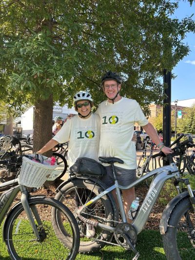 Two cyclists posing with their bikes under a tree on a sunny day.