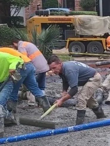The crew, using long-handled rakes, spreads and levels concrete from the ready-mix truck chute.
