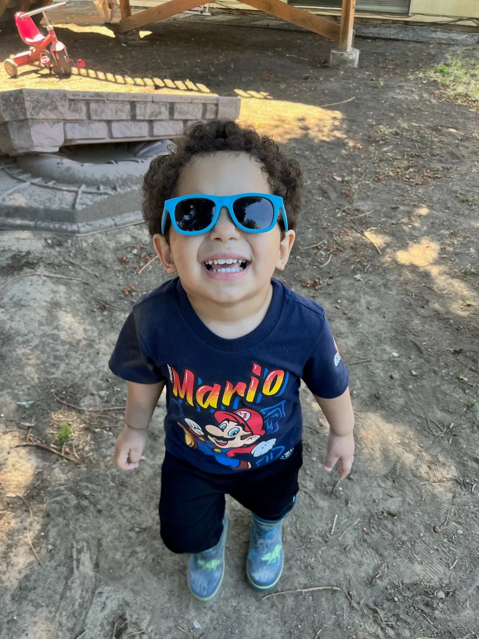 Happy kid wearing blue sunglasses and a Mario shirt.