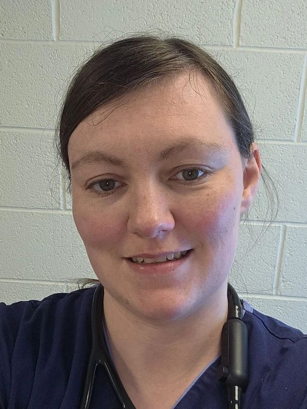 Smiling woman in navy blue scrubs with stethoscope around neck.