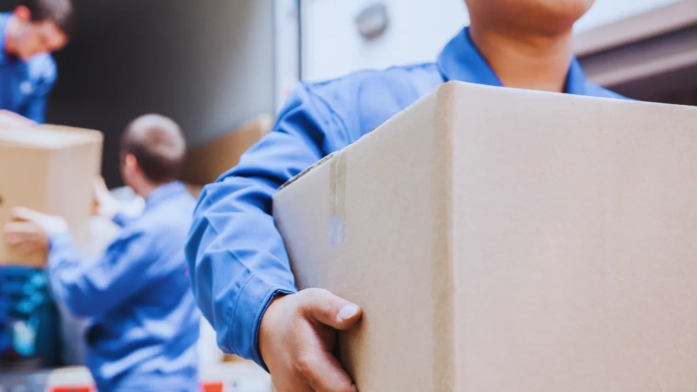 Workers in blue uniforms carrying cardboard boxes for delivery.