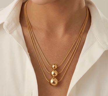 Gold triple-ball layered necklace on model's neck.