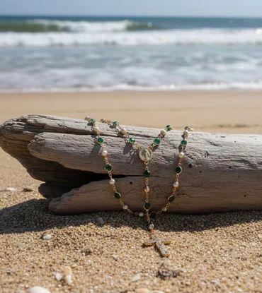 Rosary with green and pearl beads on driftwood at the beach.