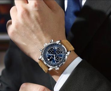 Wristwatch with a blue dial and brown leather strap on a suited wrist.