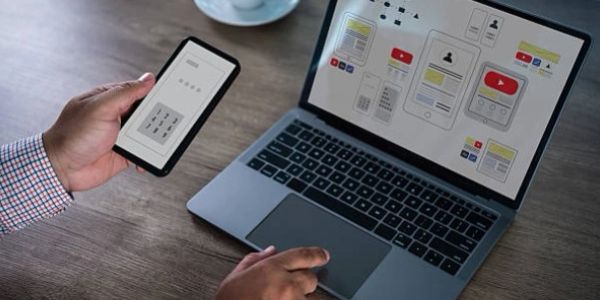 Person using phone and laptop for app design.