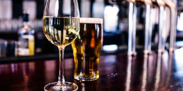 Glass of white wine and a pint of beer on a bar counter.