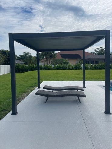 Modern pergola with two lounge chairs on a patio near a pool.