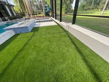Bright green artificial turf in a screened backyard with a pool and playground.