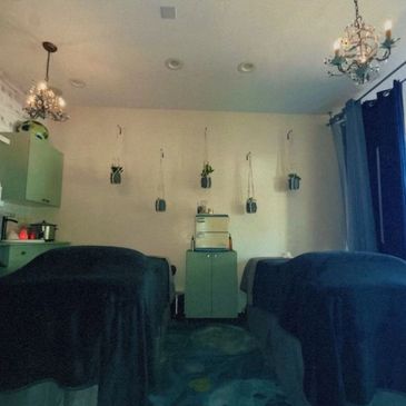 Cozy massage room with two beds and hanging plants.