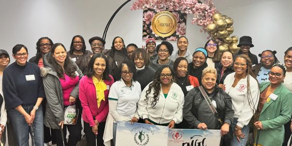 Diverse group of smiling women gathered for a community event with banners and decorations.