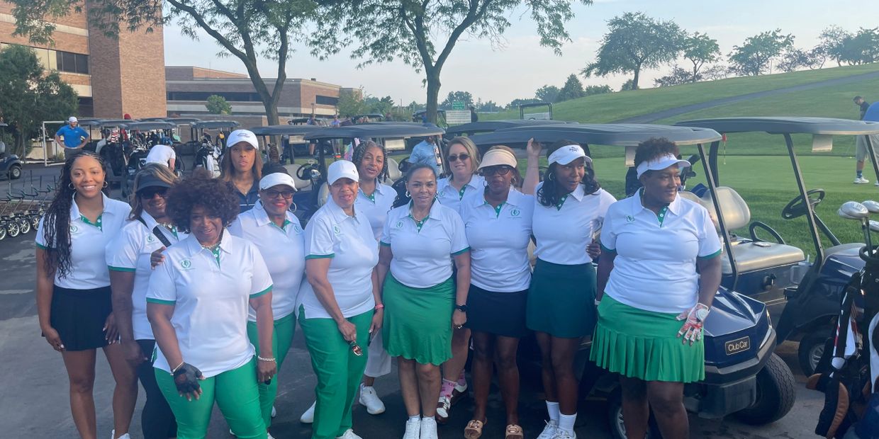 Group of women golfers posing together in matching white and green outfits beside golf carts.
