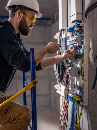 A male electrician using a screwdriver on an electrical panel.