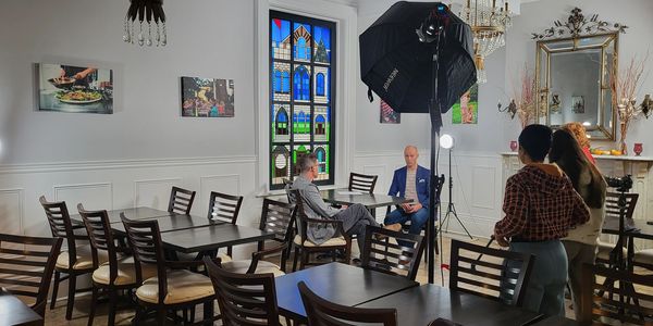 Two men being filmed in a cafe with cameras and lights.
