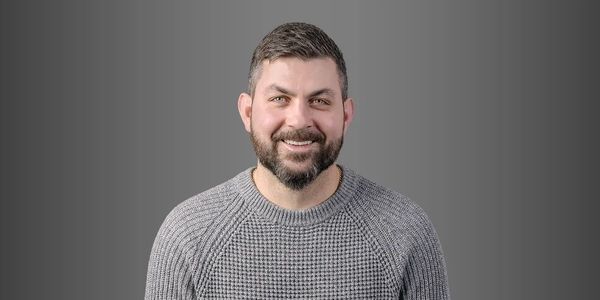 Smiling man with a beard wearing a gray sweater.