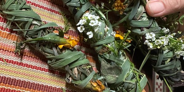 Handcrafted herbal bundles with white and yellow flowers on a woven mat.