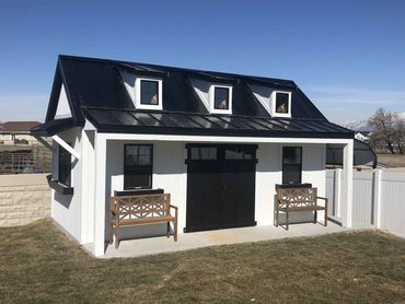 A modern white and black shed with two wooden benches on a concrete patio.