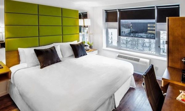 Modern hotel room with a large bed and green padded headboard.