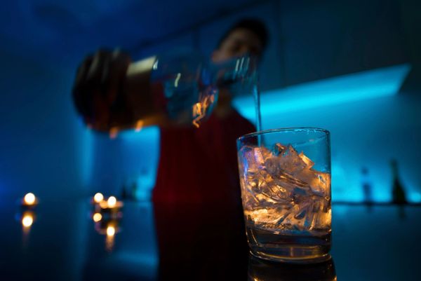 A person pouring a drink over ice in a dimly lit bar with blue ambient lighting.