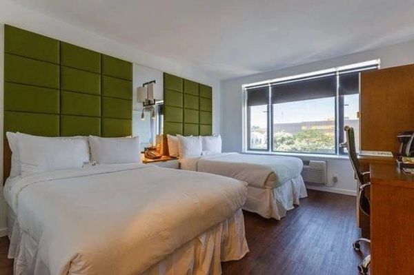 Modern hotel room with two beds and a large window.