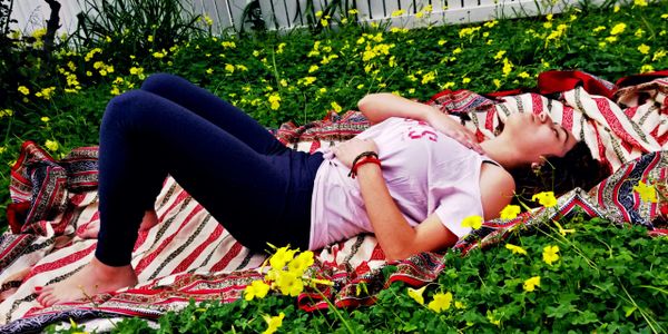 A student learning ocean breathing technique  outside laying on the grass surrounded by green grass and yellow little flowers. 