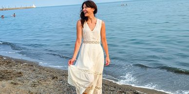 woman on beach, smiling and looking to the right wearing a white dress. 