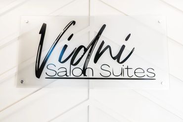 Clear sign with elegant black script reading 'Vidni Salon Suites'.