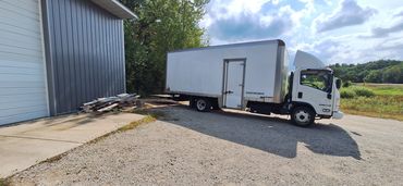 White box truck parked on gravel near a metal building under a partly cloudy sky.