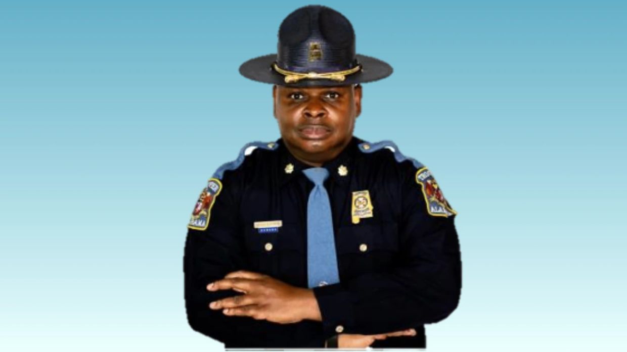 A police officer in uniform with arms crossed against a blue background.