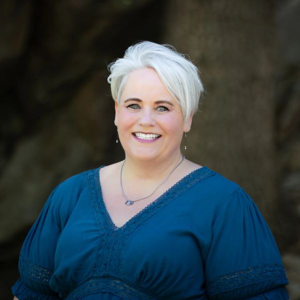 Smiling woman with short white hair in a blue top.