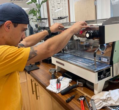 Man fixing an espresso machine with tools.