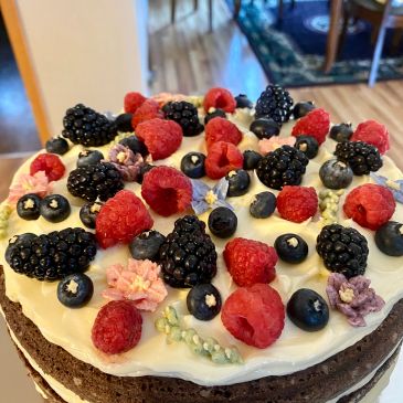 Chocolate cake topped with cream, berries, and edible flowers.