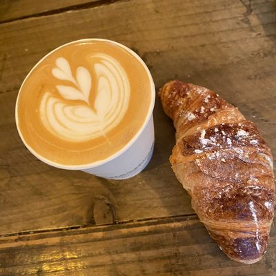 Latte art with a croissant on a wooden table.