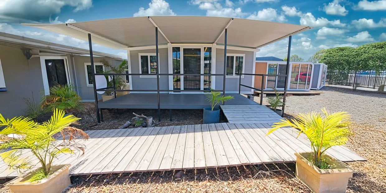 Modern modular home with a wooden deck and potted plants under a blue sky.