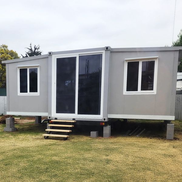 Modern gray modular home elevated on concrete blocks with large glass doors and windows.