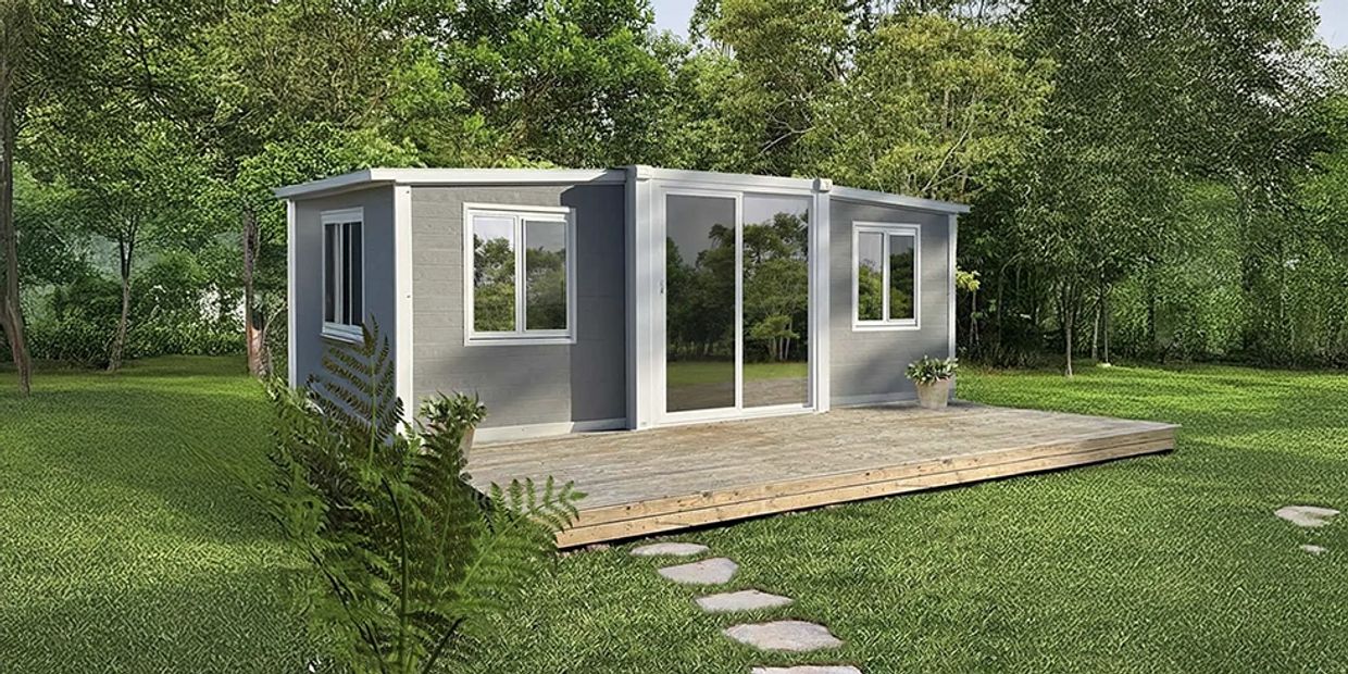 Modern tiny house with large windows and wooden deck in a lush green setting.
