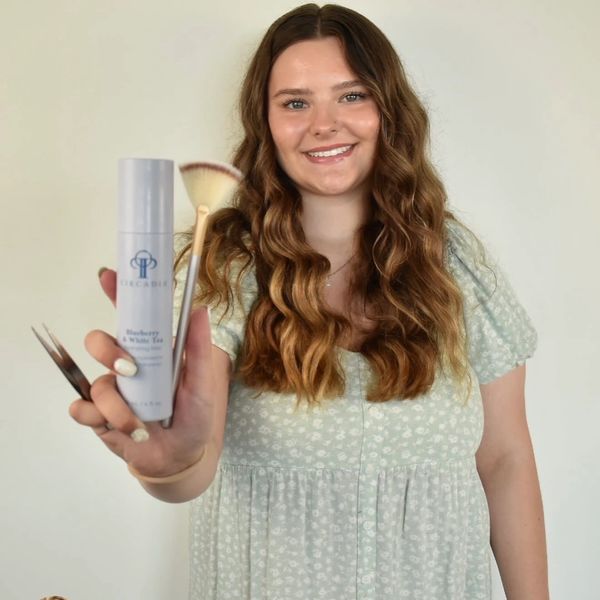 Smiling woman holding beauty products and brushes.