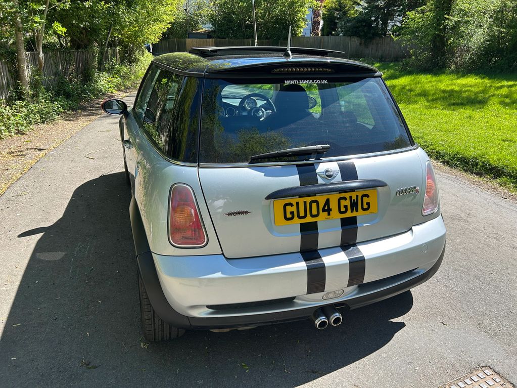 Rear view of a silver Mini Cooper S with black racing stripes parked on a sunny road.