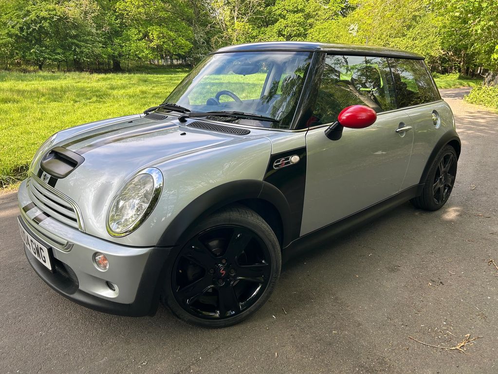 Silver Mini Cooper S with black wheels and red side mirrors parked on a road.