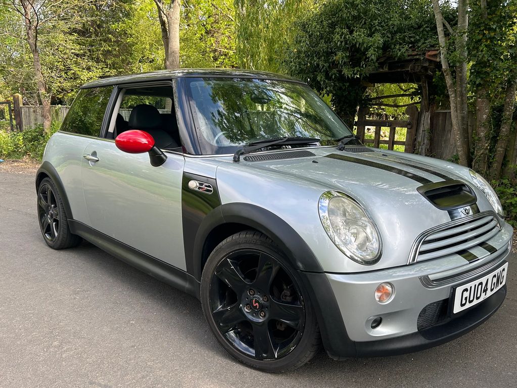 Silver Mini Cooper with black stripes and red side mirrors parked on a road.