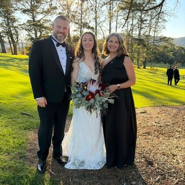 A bride with two people in formal wear outdoors.