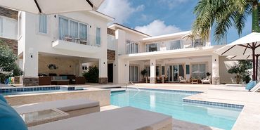 Modern white villa with pool, lounge chairs, and palm trees under a blue sky.